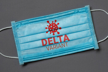 A blue medical face mask lies on a dark grey background with the inscription delta variant,...
