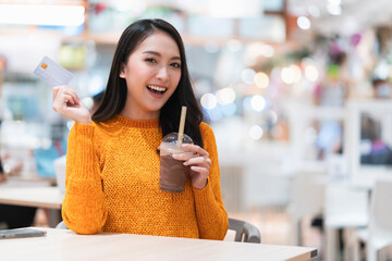smiling asian female hand hold ice coffee drink sit relax casual at cafeteria food court department store mall,asian female hand hold credit card cashless lifestyle shopping ideas concept