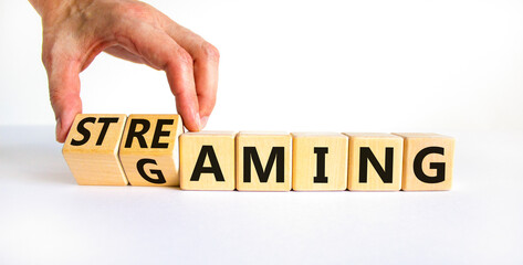 Gaming and streaming symbol. Businessman turns wooden cubes and changes the word gaming to streaming. Beautiful white table white background, copy space. Business, gaming and streaming concept. © Dzmitry
