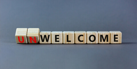 Welcome or unwelcome symbol. Turned wooden cubes and changed the word unwelcome to welcome. Beautiful grey table, grey background. Welcome or unwelcome and business concept. Copy space.