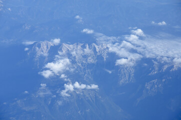 Beautiful window view of blue sky, fluffy clouds and Alps mountains from passenger seat on airplane. Travel and air transportation. Holidays