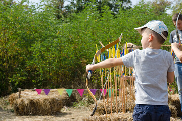 Little boy, kid with bow and arrow aiming at archery target in park, back view. Outdoor sport, activity. Family time. 