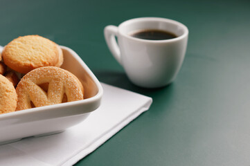 Espresso coffee and butter cookies in porcelain bowl. Isolated on green background with copy space.