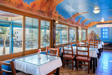 Interior of a fish restaurant decorated in a blue colour. Spacious restaurant hall is empty, there are no visitors at the tables. Large windows offer city views