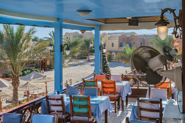 Interior of a fish restaurant open terrace decorated in a blue colour. Spacious restaurant hall is empty, there are no visitors at the tables. Terrace offers city views