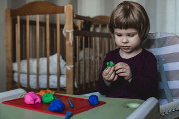 Cute little child plays with modelling clay at home.