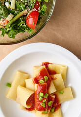 Flat lay. Cropped photo of a healthy vegan meal consisting of vegetarian herb salad and cooked italian pasta with tomato sauce and green onion garnish
