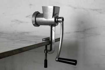 Metal manual meat grinder on table against white marble background