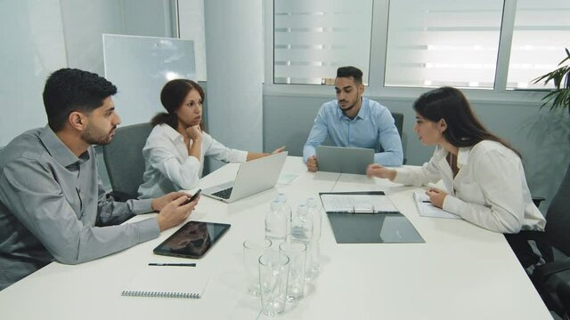 Young indian team leader sitting with colleagues, discussing issues at negotiations meeting. Skilled millennial diverse employees working together at office developing startup marketing strategy