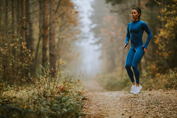 Young woman taking high jump on the forest trail at autumn