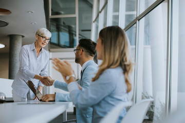 Fototapeta premium Mature business woman handshaking with young colleague on a meeting in office