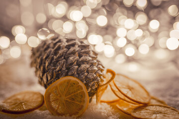 Karta świątecznan  z szyszką, pomarańczą na tle z światełek bokeh.