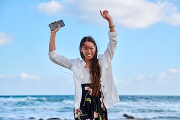 Beautiful woman in headphones with smartphone dancing on the beach