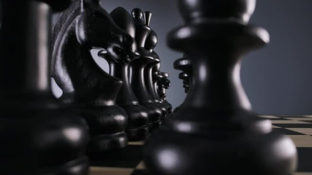 Close-up of wood chessboard with lines of black wooden chess figures in a row ready to play with blurred foreground and background. Slider move. 4K