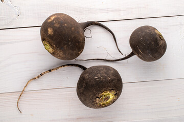 Three ripe organic black radishes on a wooden table, close-up, top view.