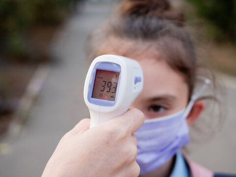 Temperature measurement of a sick child with a non-contact digital infrared thermometer showing fever. Schoolgirl girl with high fever. Pandemic, flu epidemic concept.