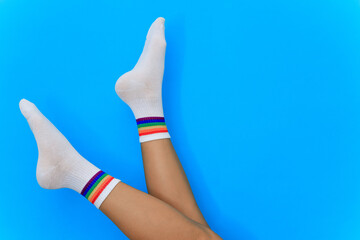 legs of woman with pair of white cotton socks with rainbow stripes on blue background isolate