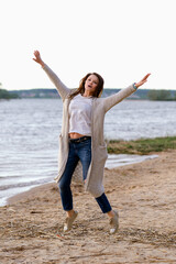 fashionable girl in trousers, blouse walks on the shore of the lake. sunset. girl jumping and having fun on the seashore