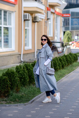 Obraz premium a fashionable girl in trousers, a raincoat, a blouse with a handbag walks around the city. Business concept