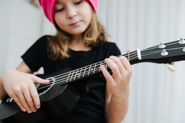 Focused pretty little girl in a pink winter hat playing on a guitalele