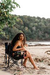 Hermosa mujer latina sentada en una silla en la playa con su mascota, sonriendo viendo a cámara