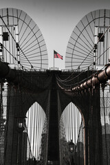 Obraz premium The national flag of United States of America winding on top of Brooklyn Bridge landmark from Manhattan. One of the most visited places in America. Symbol of patriotism.