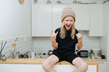 Hyped pumped boy sitting on a high table, showing rock'n roll gesture