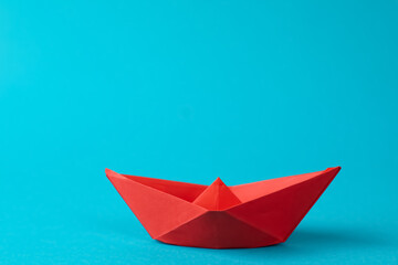 Handmade red paper boat on light blue background.  Origami art