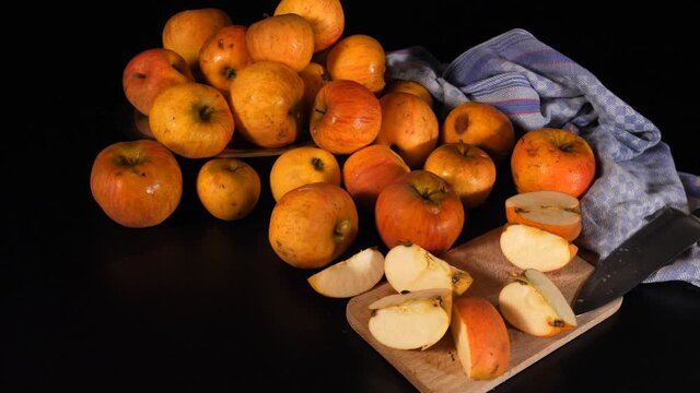 Frische orangefarbene Bio- &Auml;pfel mit Macken, B-Ware, zum Teil zerschnitten, Apfelschalen, Messer, Brettchen und blaues K&uuml;chentuch. Kamerafahrt