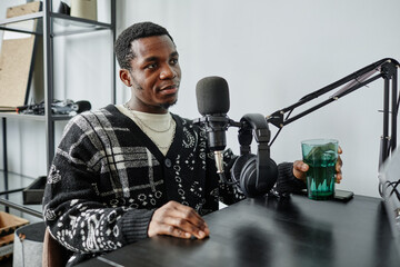 Portrait of African-American man speaking to microphone while recording podcast in studio