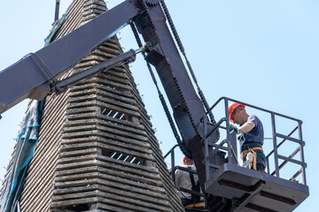 A tower crane with a cradle lifts people to perform work on repairing the roof of the old historical knowledge. Replacement of roof tiles. Performing installation work at height.