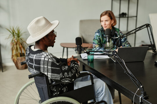 Portrait of young female creator interviewing person with disability while recording podcast