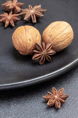 Star anise and walnuts on black plate.