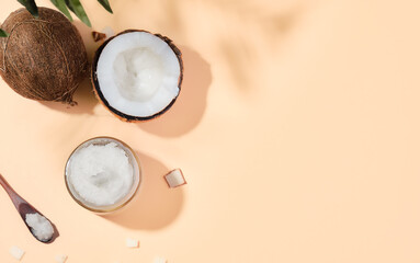 Coconut oil in a jar and coconuts on a colored background, the shadow he leaves of a palm tree on the table, bright sunlight. Top view with copy space. Organic coconut oil