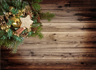 Christmas decoration of spruces twigs decorated with a glass golden balls, star, boubles and pine cones on a grunge wooden background with copy space