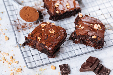 Chocolate brownies with hazelnut crumbs on top, on a tray with cacao powder, chocolate crumbs on a white rustic background. Very fudge brownies