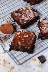 Chocolate brownies with hazelnut crumbs on top, on a tray with cacao powder, chocolate crumbs on a white rustic background. Very fudge brownies
