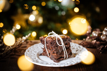 Fototapeta na wymiar Chocolate brownies wrapped in group as a present in front of Christmas tree with Christmas lights in festive atmosphere and decoration