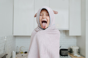 Happy funny little girl wrapped in a bear hooded towel sticking tongue out