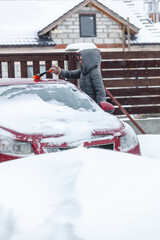 Young woman brushing snow from car after heavy snowfall