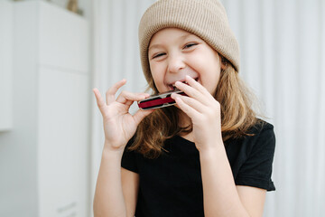 Cheeky little girl in a beige hat playing with a harmonica, smiling
