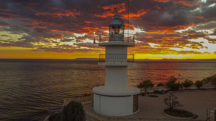 Faro marítimo sobre atardecer rojizo con el mar en calma de poniente
