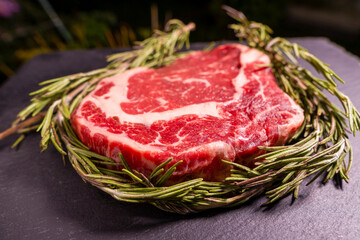 Raw marbled beef steak on a stone tray with rosemary. close-up.