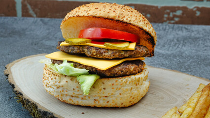 Delicious double tasty hamburger with beef cutlet,  fresh vegetables and  2 slices of cheddar cheese on vintage wooden tray with brick wall background