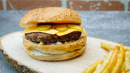 cheeseburger  with cheddar chese, russian salad, pickled cucumbers, french fries on wooden tray with brick wall background