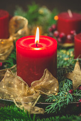 Burning red candle in an advent arrangement with fresh fir branches, first advent, vertical