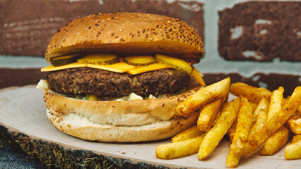 cheeseburger  with cheddar chese, russian salad, pickled cucumbers, french fries on wooden tray with brick wall background