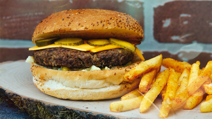 cheeseburger  with cheddar chese, russian salad, pickled cucumbers, french fries on wooden tray with brick wall background