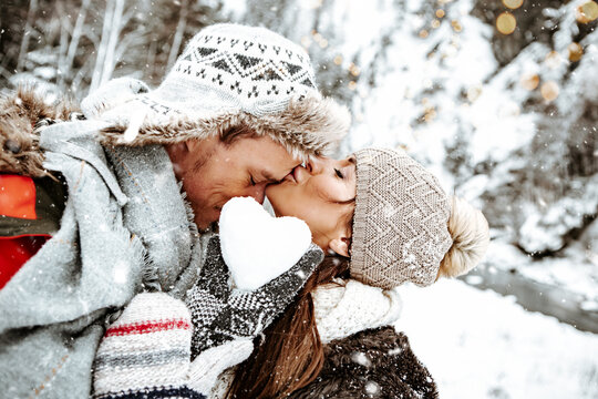 young,attractive european couple kissing in front of beautiful snowy winter landscape in the mountains. couple holding a heart made of snow in their hands.