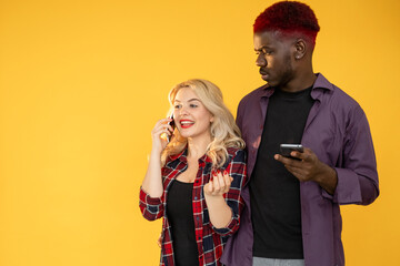 Mobile conversation. Great news. Unexpected call. Relationship jealousy. Multiracial diverse couple of happy woman talking on phone with suspicious Afro man on orange empty space.